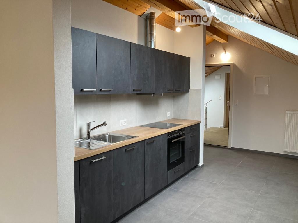 Modern kitchen with grey cabinets, wooden countertop, stainless steel sink and faucet, built-in oven, and exposed wooden beams on the ceiling.