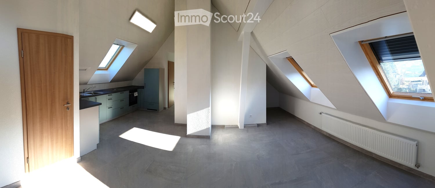 Bright, open attic space with exposed wooden beams, skylights, and a small kitchen area with cabinets and appliances.