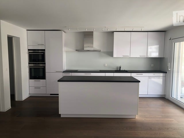 Modern kitchen with white cabinets, black countertops, and a central island. Features include built-in ovens, a sink, and ample storage space.