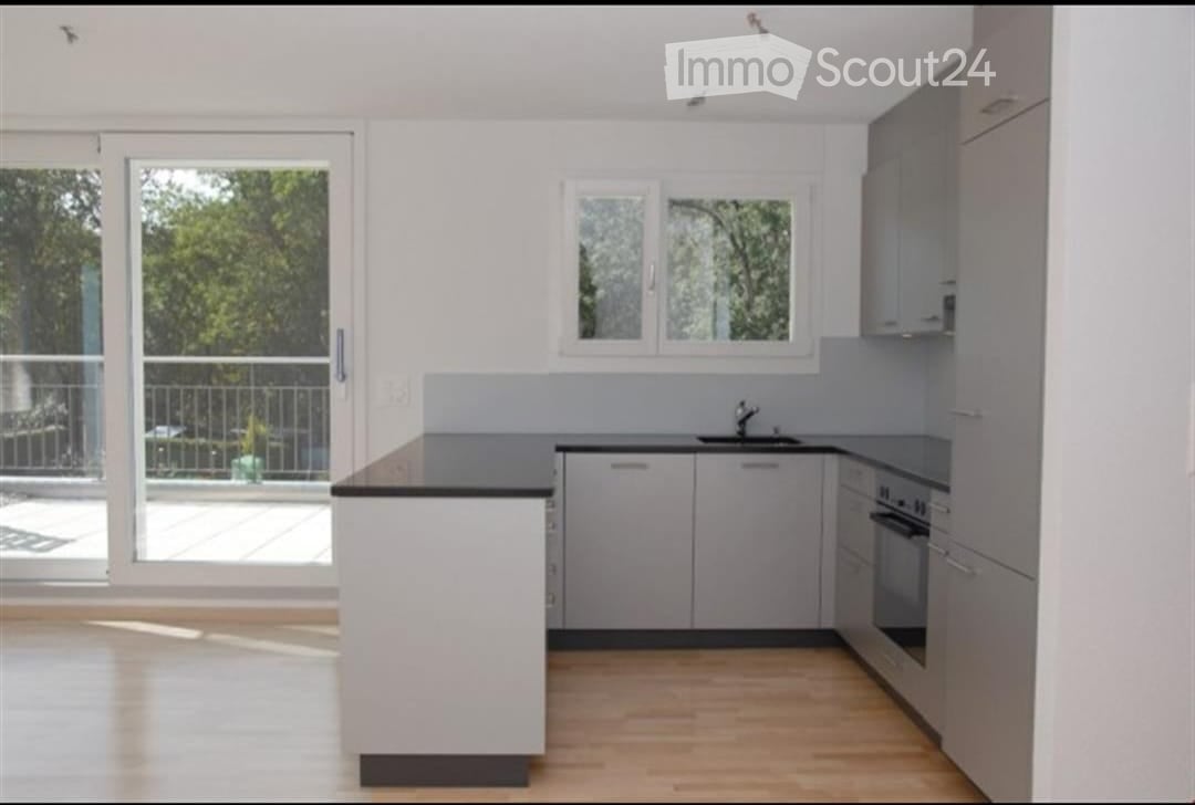 Modern kitchen with grey cabinets, a central island, and large windows overlooking a balcony.