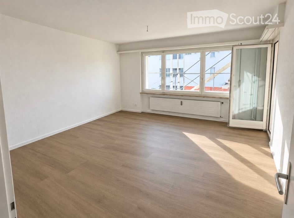 Empty room with wooden flooring, white walls, large windows, and a radiator. No furniture or equipment present.