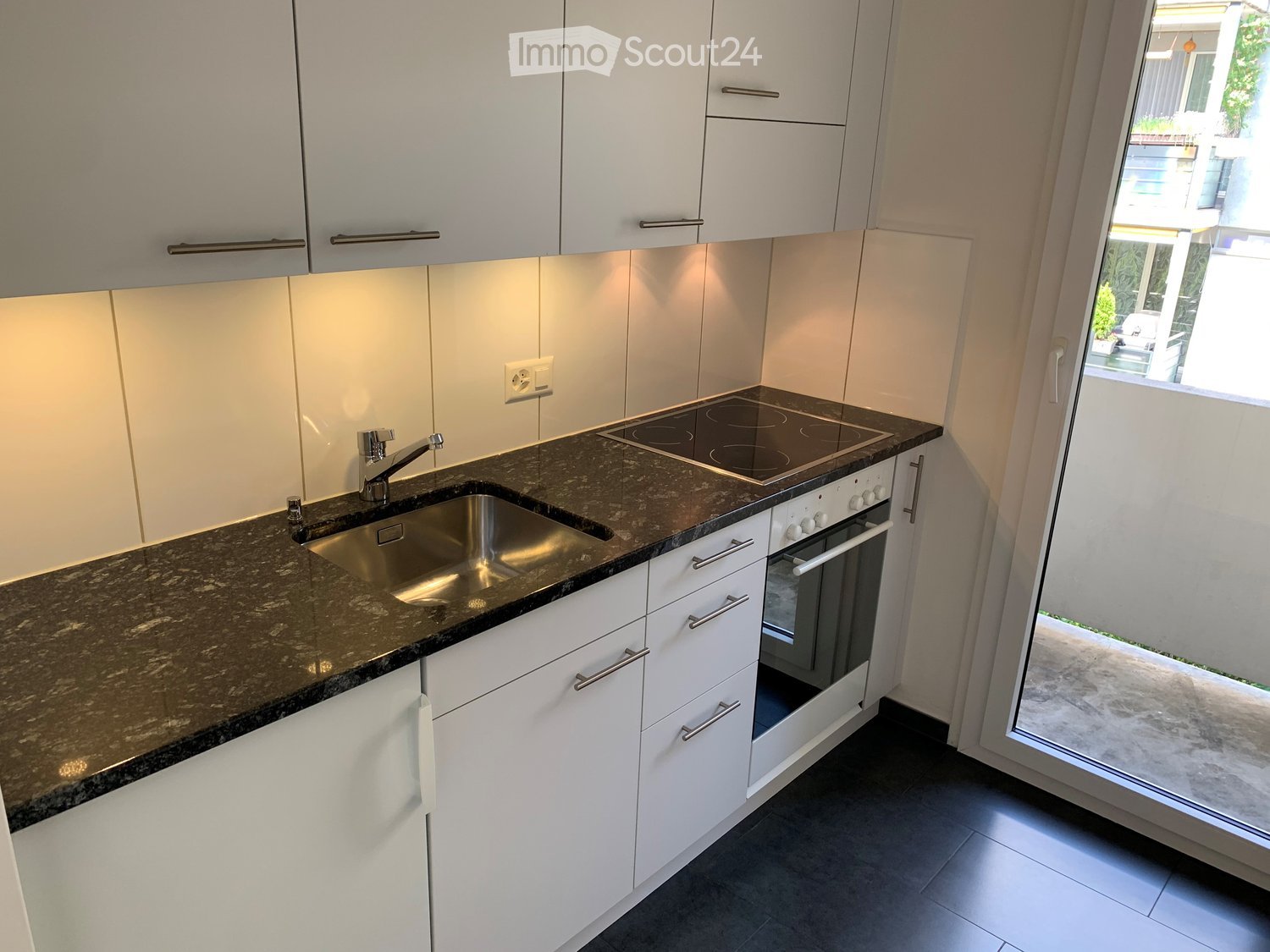 Modern kitchen with white cabinets, granite countertop, stainless steel sink, induction cooktop, and built-in oven.
