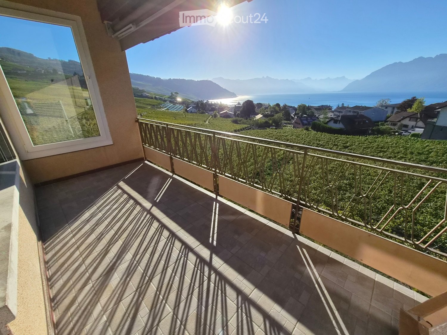 Balcony with tiled floor, metal railing, and scenic view of vineyards, lake, and mountains.