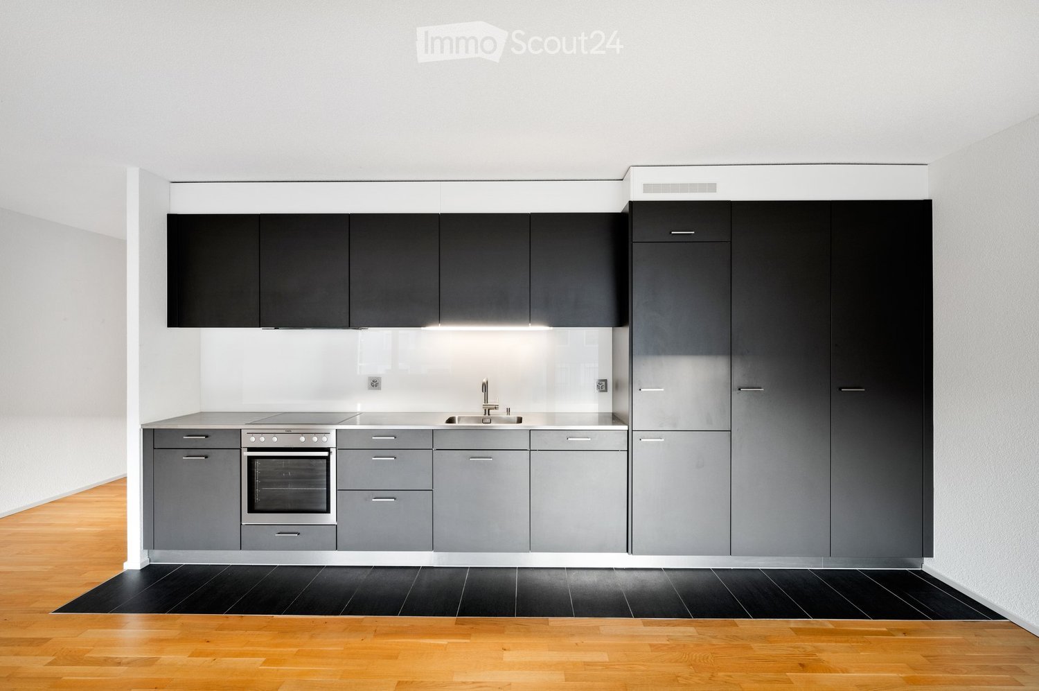 Modern kitchen with grey cabinets, stainless steel oven, sink, and faucet, featuring a black tiled floor and wooden flooring.