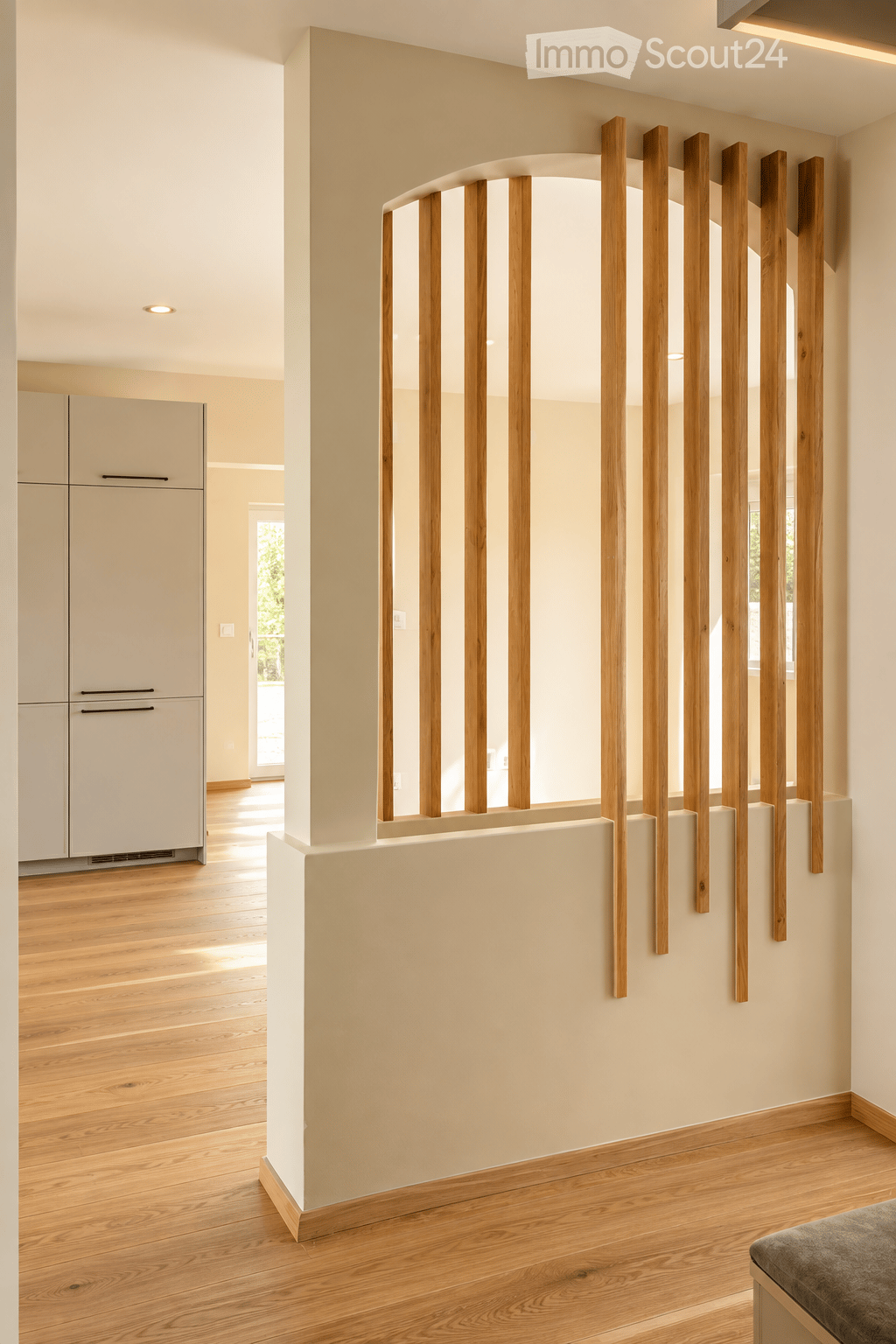 Modern hallway with light wooden flooring, white walls, and a decorative wooden partition with vertical slats. A grey cabinet is visible in the background, and a grey cushioned bench is partially visible in the foreground.