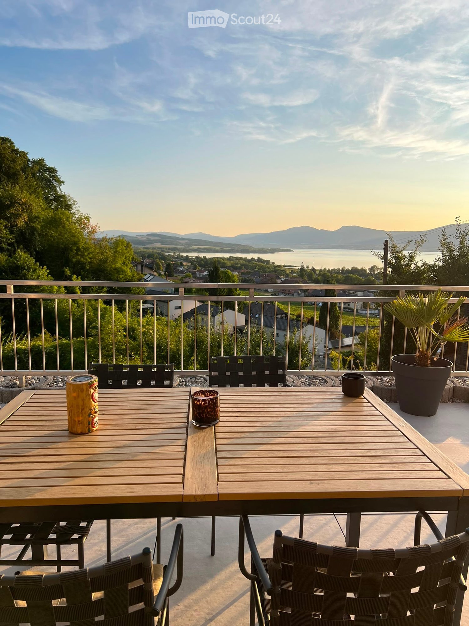 Balcony with wooden table, black chairs, and scenic view of a lake and mountains.