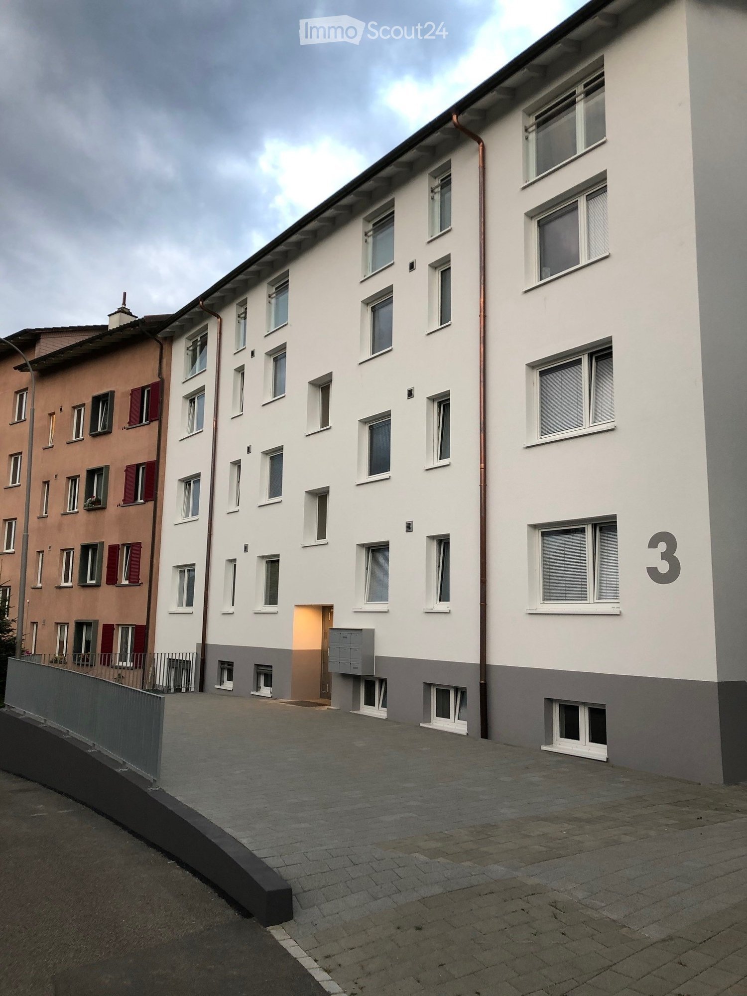 Multi-story residential building with white facade, multiple windows, and a raised ground floor entrance.