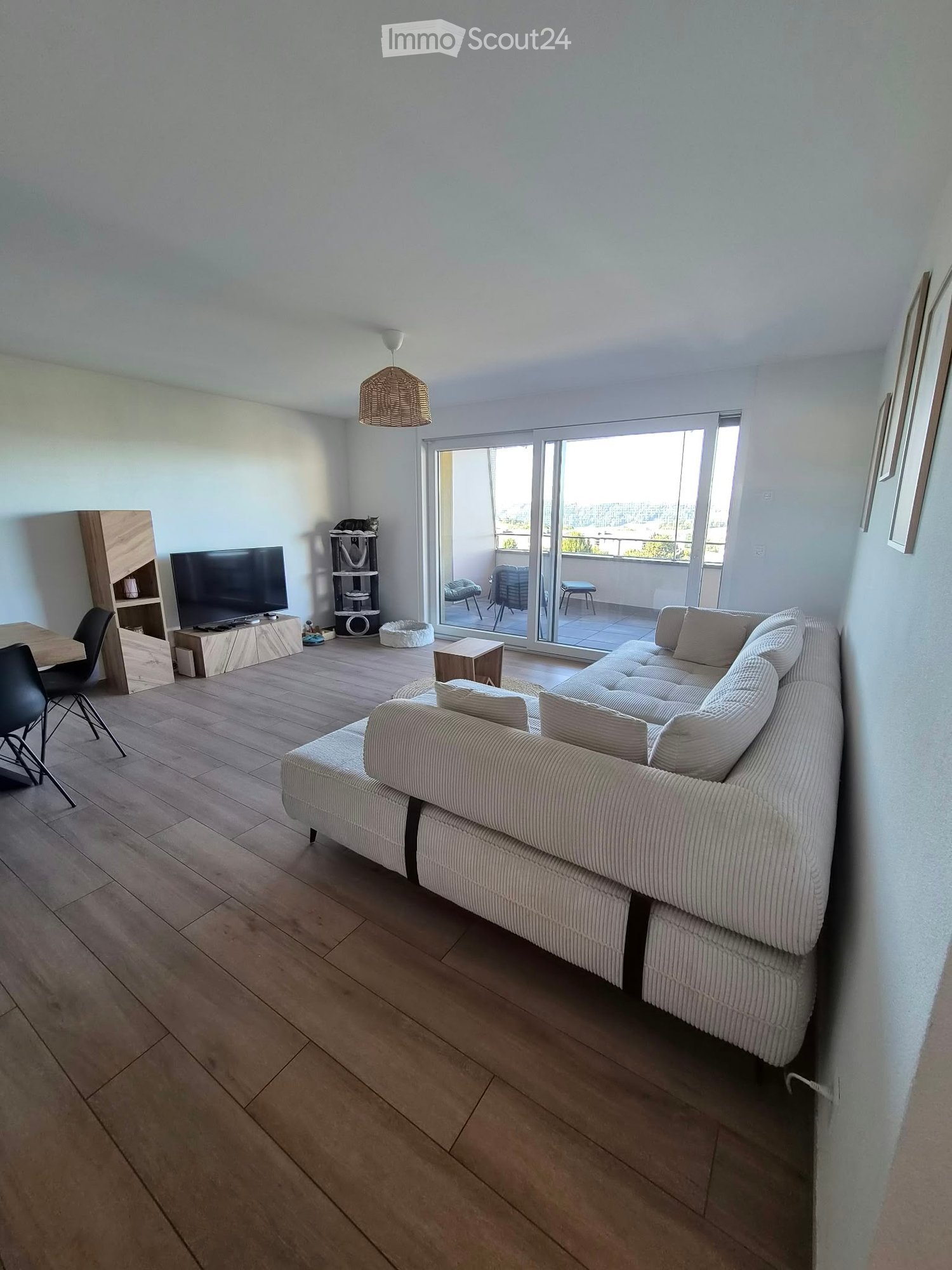 Modern living room with a large sectional sofa, coffee table, dining area, cat tree, and access to a balcony.