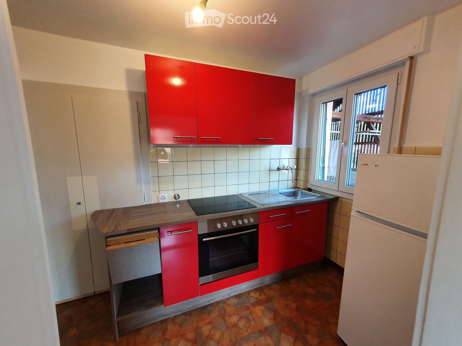 Modern kitchen with red cabinets, stainless steel oven, sink, and refrigerator. Features tiled backsplash and wooden countertop.