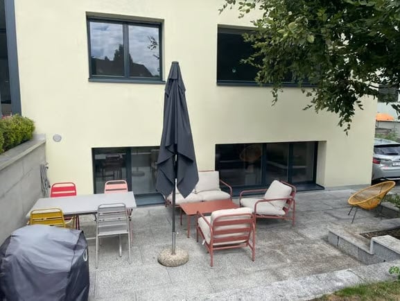 Outdoor patio area with a table, chairs, and an umbrella near a building entrance.