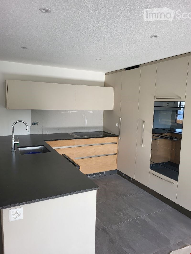 Modern kitchen with light-colored cabinets, black countertop, stainless steel sink and faucet, built-in oven, and wooden drawers.