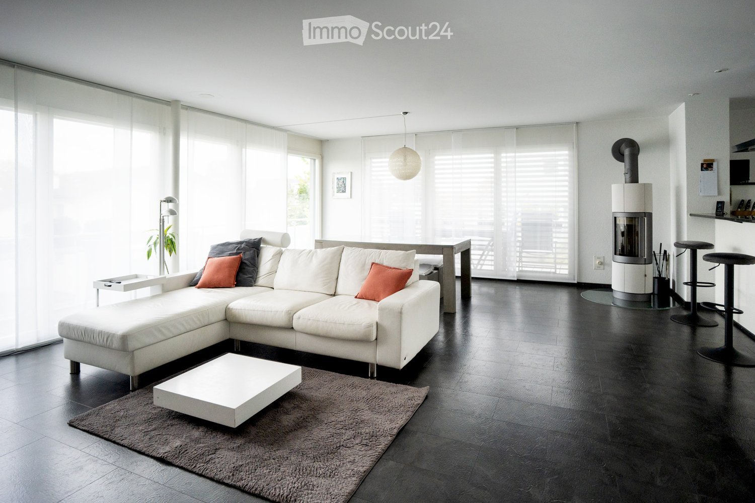 Modern living room with white sectional sofa, coffee table, fireplace, and large windows with blinds.