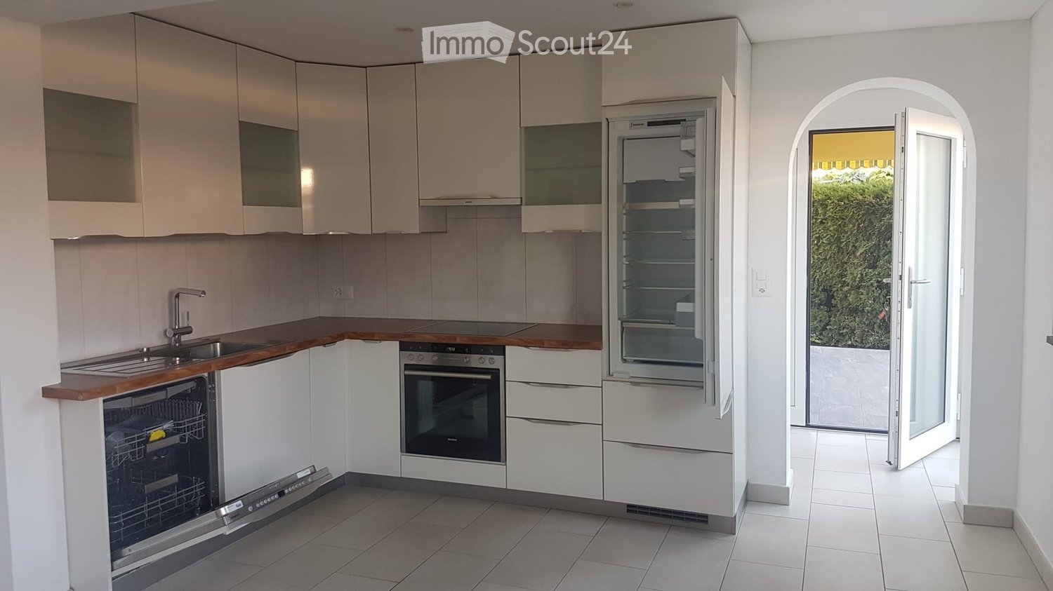 Modern kitchen with white cabinets, wooden countertops, stainless steel appliances, and an open doorway leading outside.