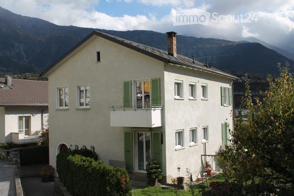 Two-story house with white walls, green shutters, and a balcony overlooking a scenic mountain view.