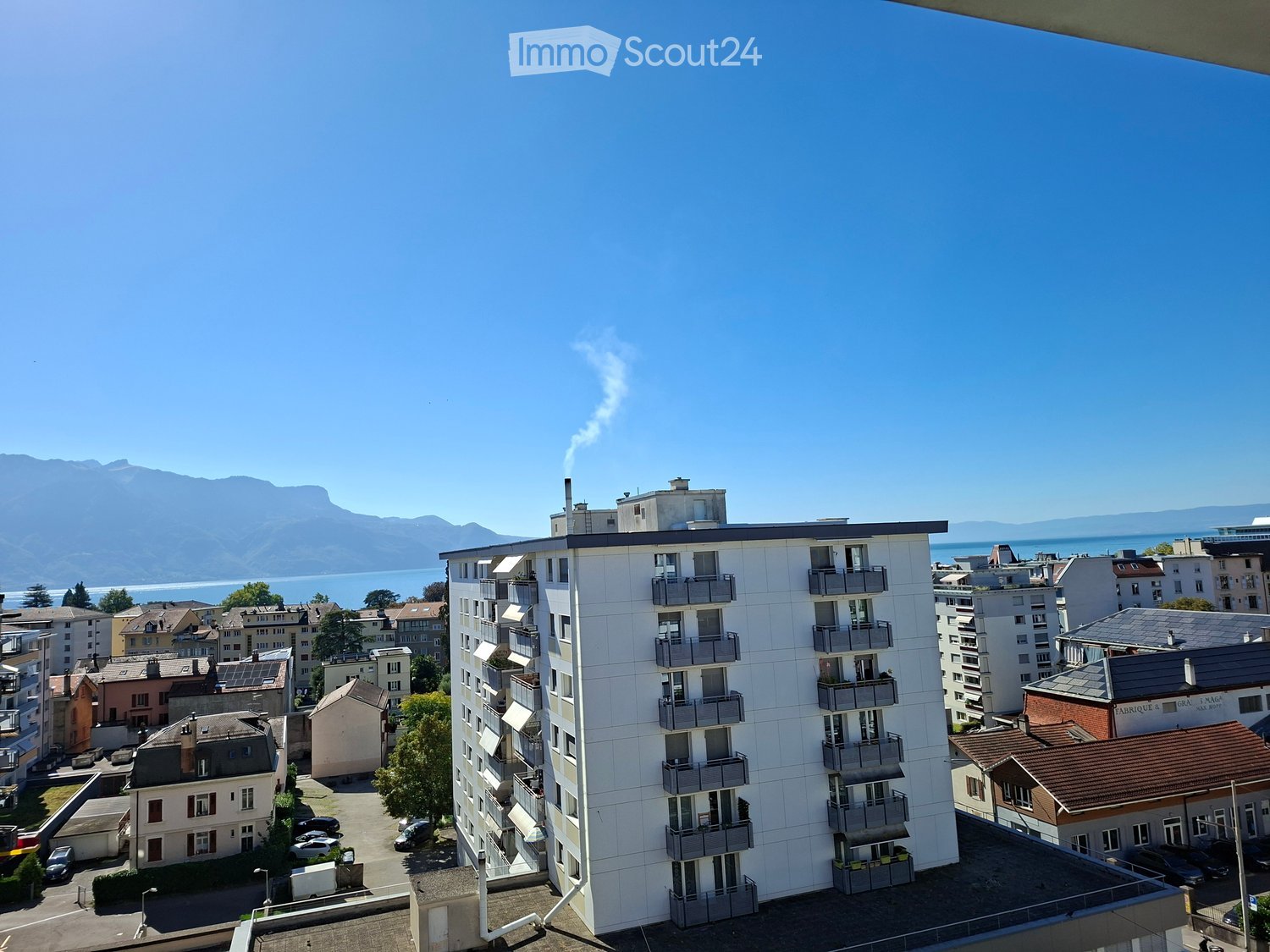 A modern multi-story apartment building with balconies overlooking a scenic view of a lake and mountains.