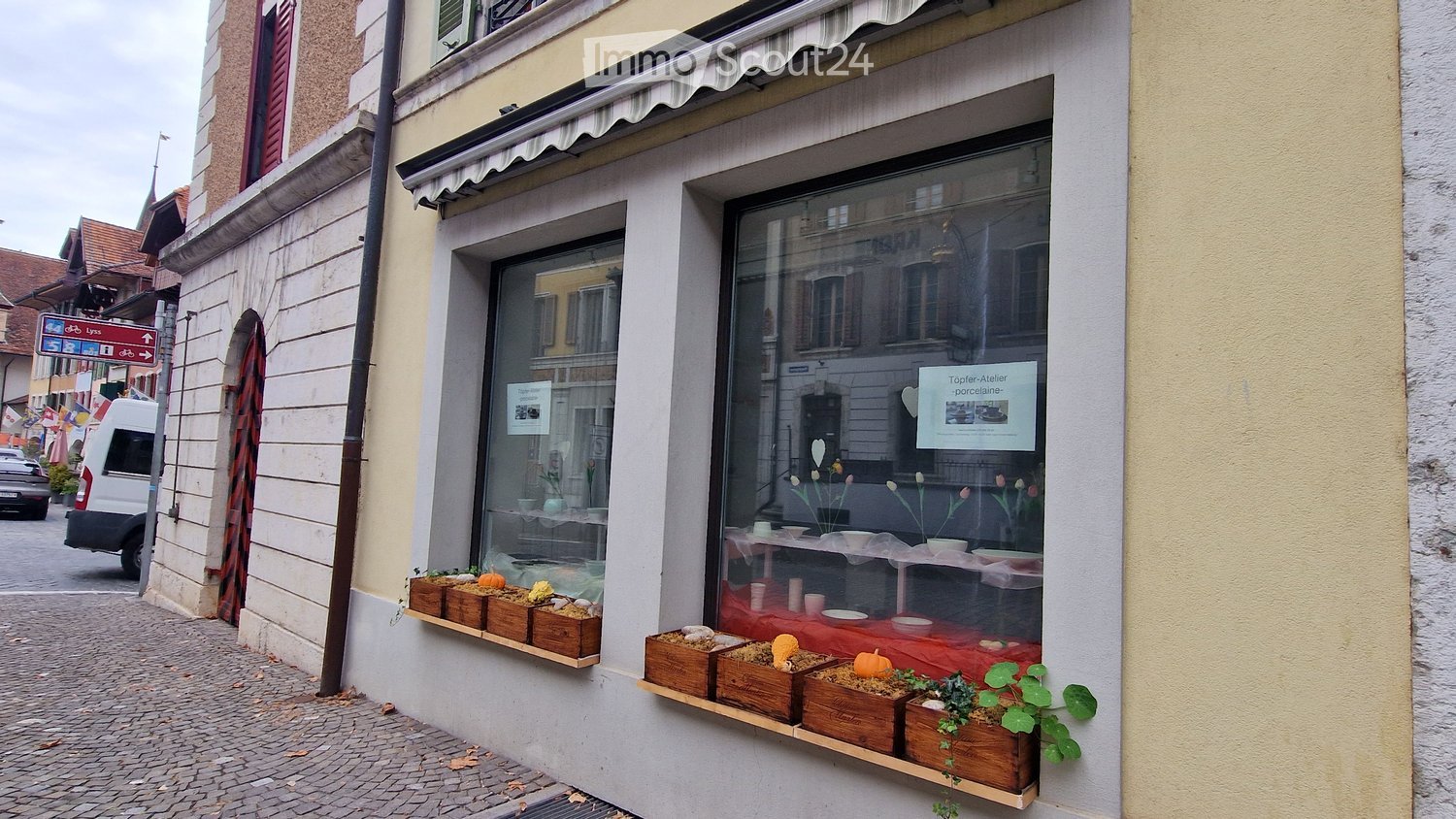 Facade of a building with a storefront displaying ceramic items and decorative plants in wooden boxes on a ledge.