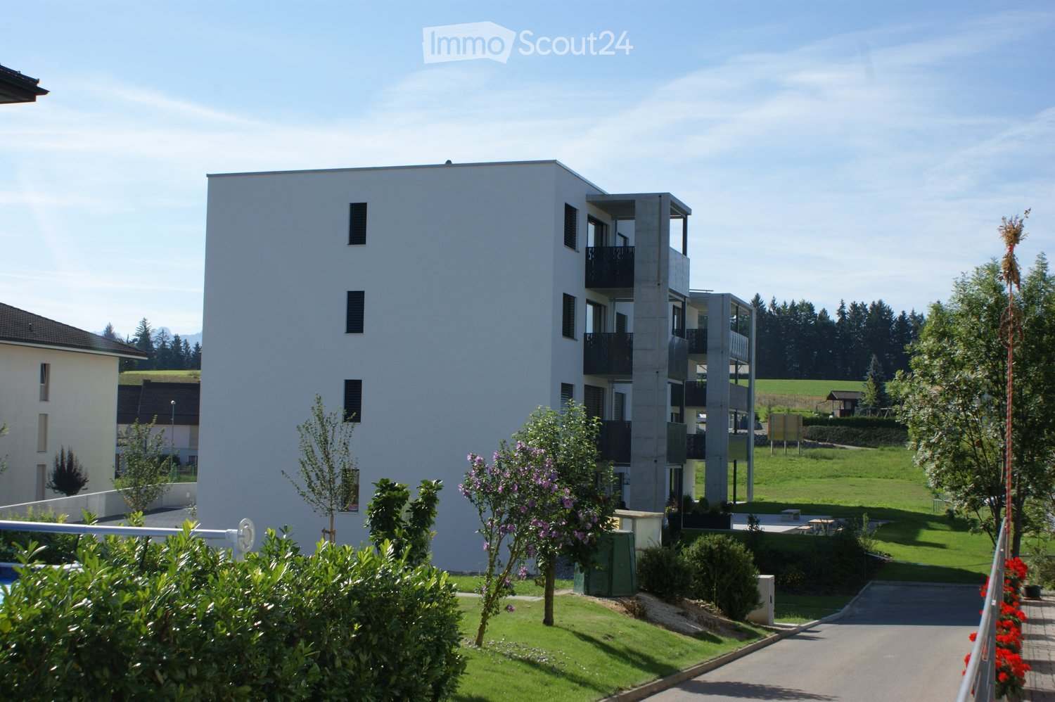 Modern multi-story residential building with balconies, surrounded by greenery and a well-maintained lawn.