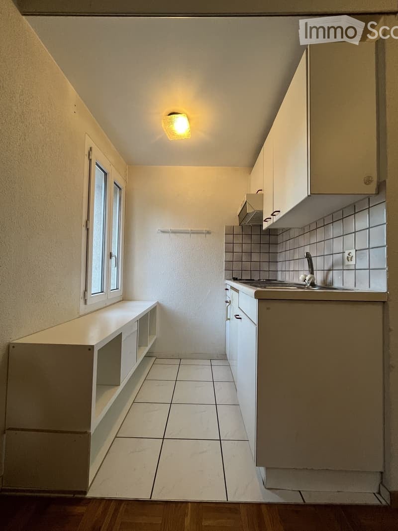 Empty kitchen with white tiled floor, white cabinets, and a window. The space includes a sink with a faucet and a built-in bench with storage compartments.