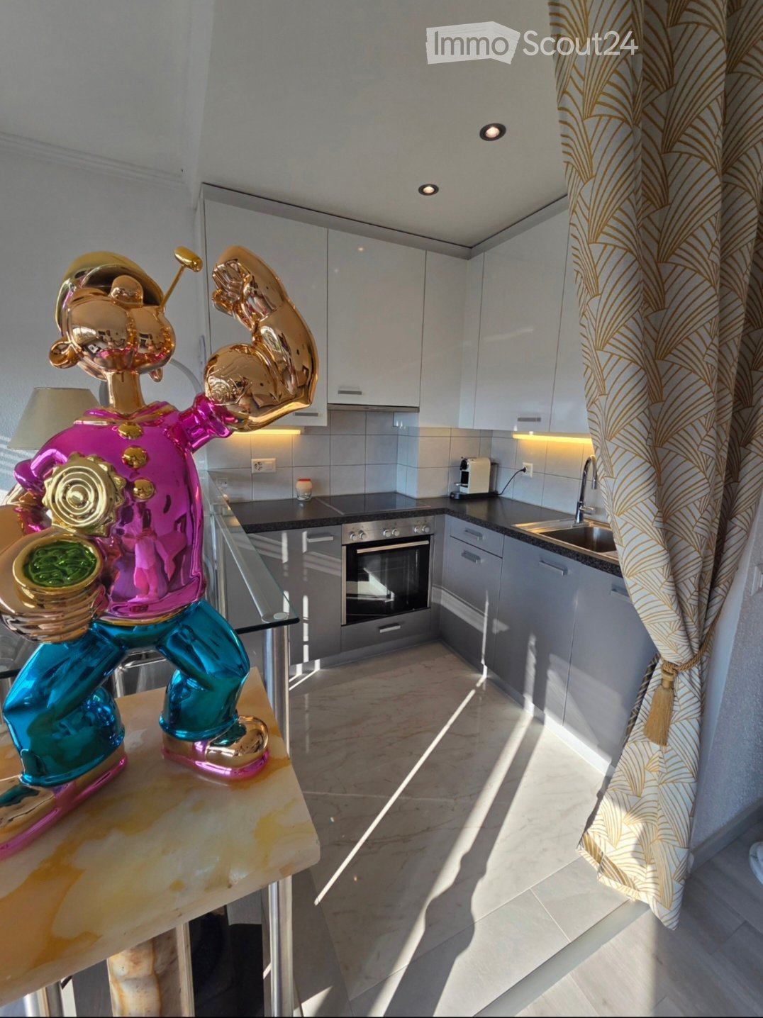 Modern kitchen with white cabinets, stainless steel appliances, marble countertops, and a decorative golden sculpture on a table.