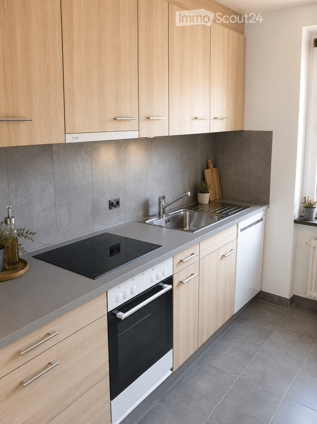 Modern kitchen with light wooden cabinets, stainless steel appliances, grey countertops, and a small potted plant on the windowsill.