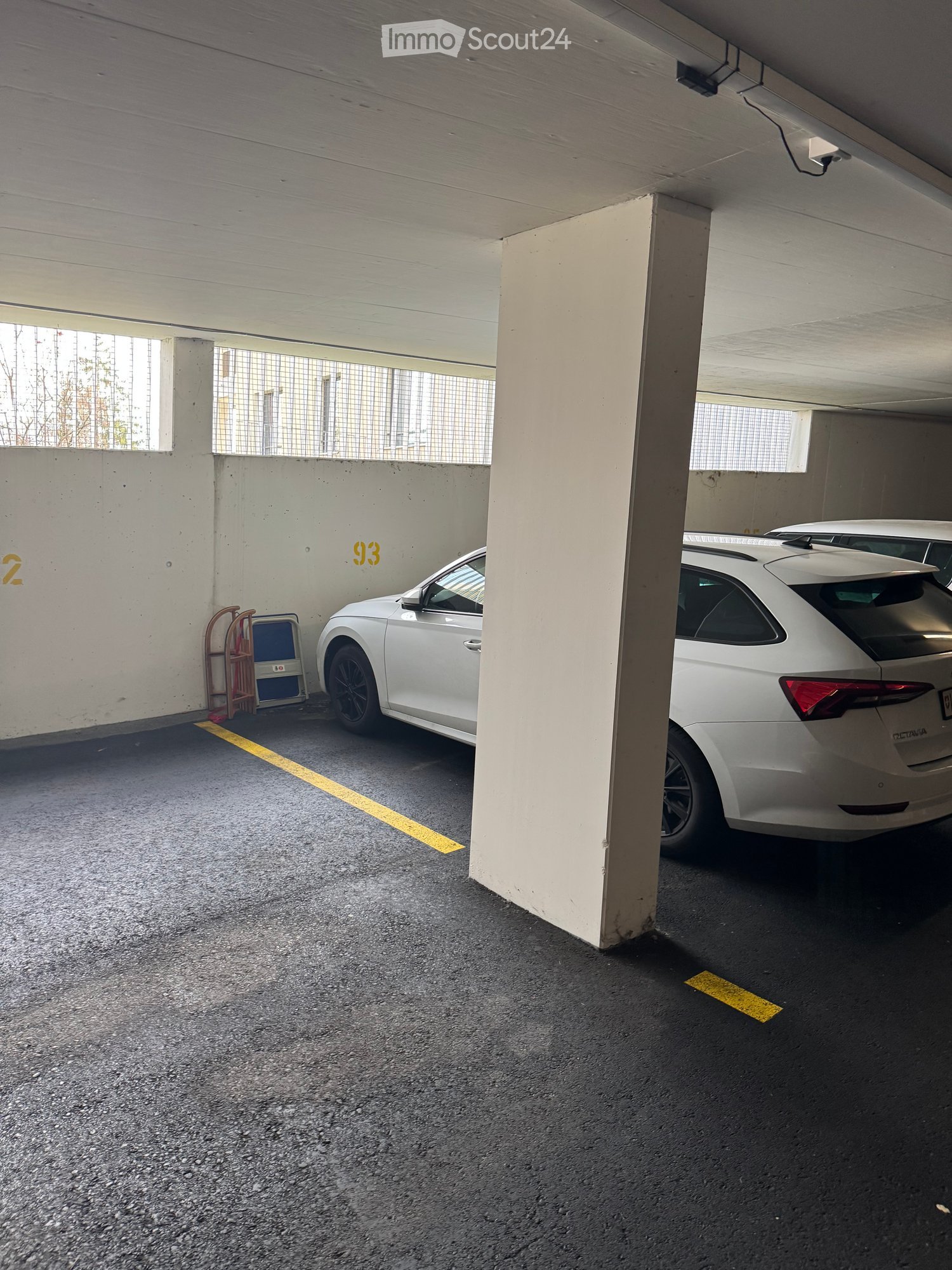 Underground parking area with two white cars parked, concrete pillars, and numbered sections.