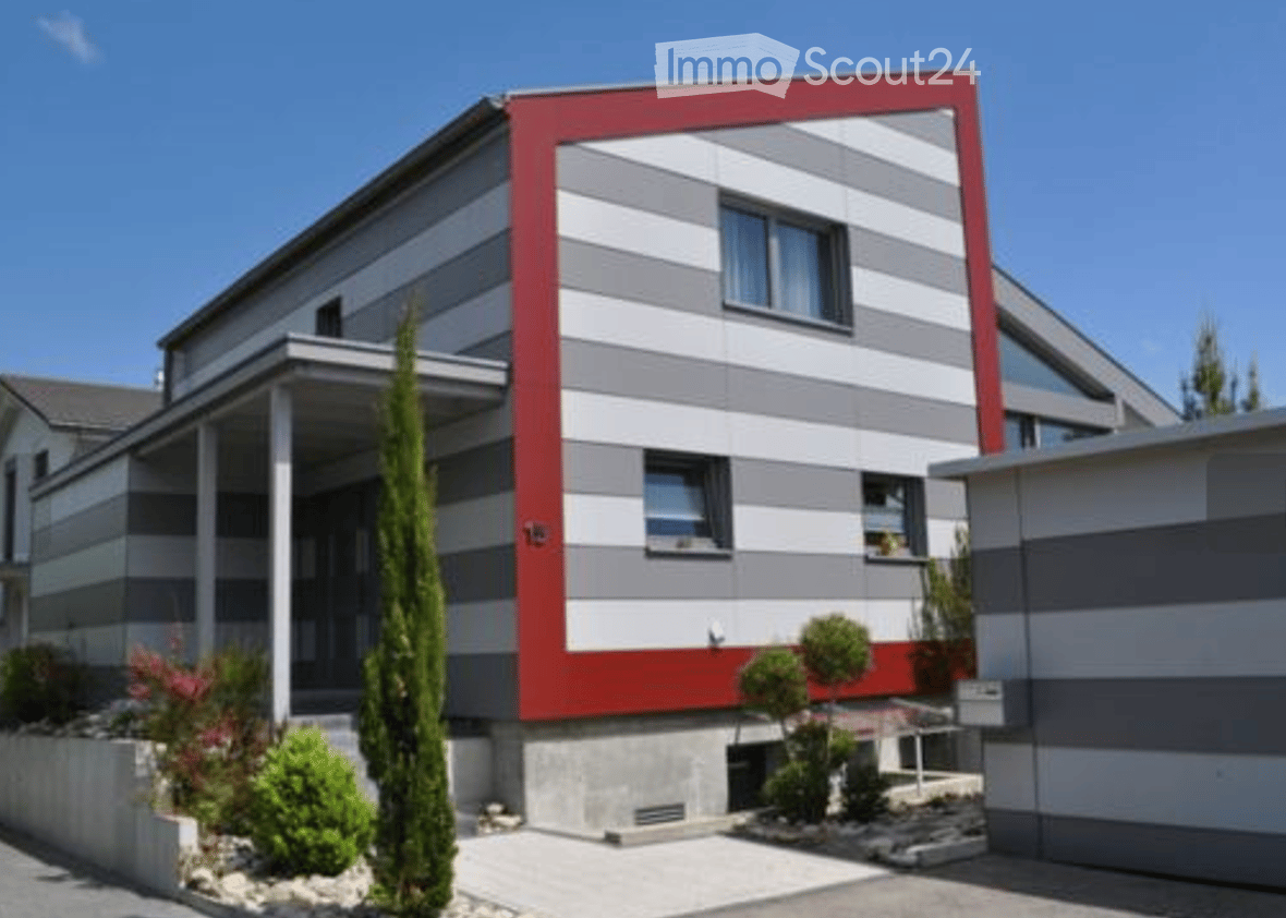 Modern two-story house with red and grey exterior, large windows, and a small garden area.