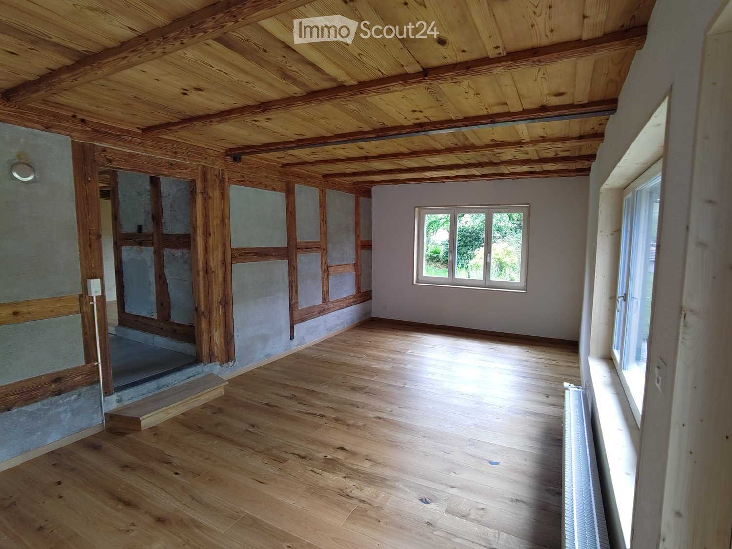 Unfurnished Room. Empty room with wooden ceiling, wooden flooring, and white walls. Two windows with wooden frames and a power outlet on the wall.
