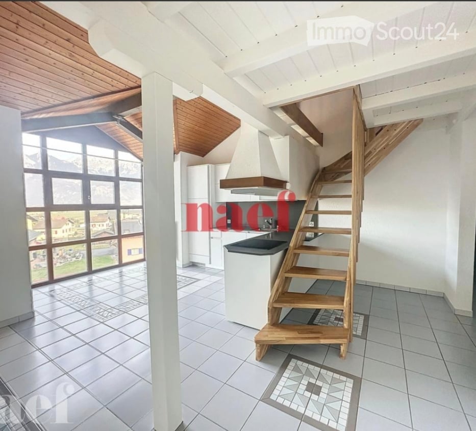 Bright kitchen with large windows offering a scenic view, featuring a wooden staircase leading upwards, a sink, a refrigerator, and a range hood.