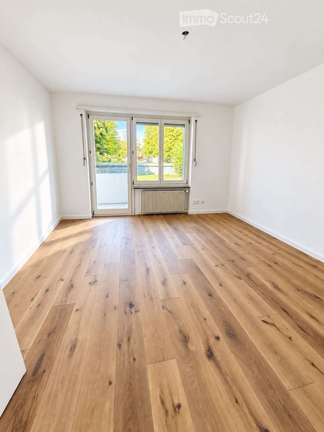 Empty room with light wooden flooring, white walls, and a large sliding glass door leading to a balcony or outdoor area.