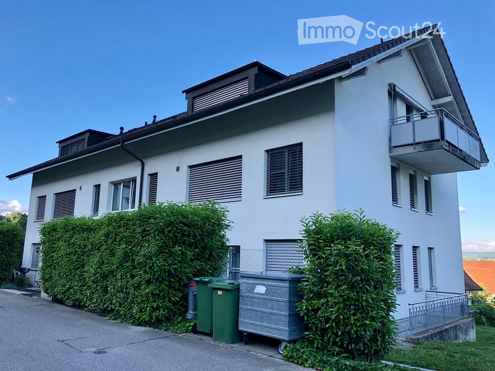 White painted exterior, rectangular windows, small balcony on the top floor, and a fence in front
