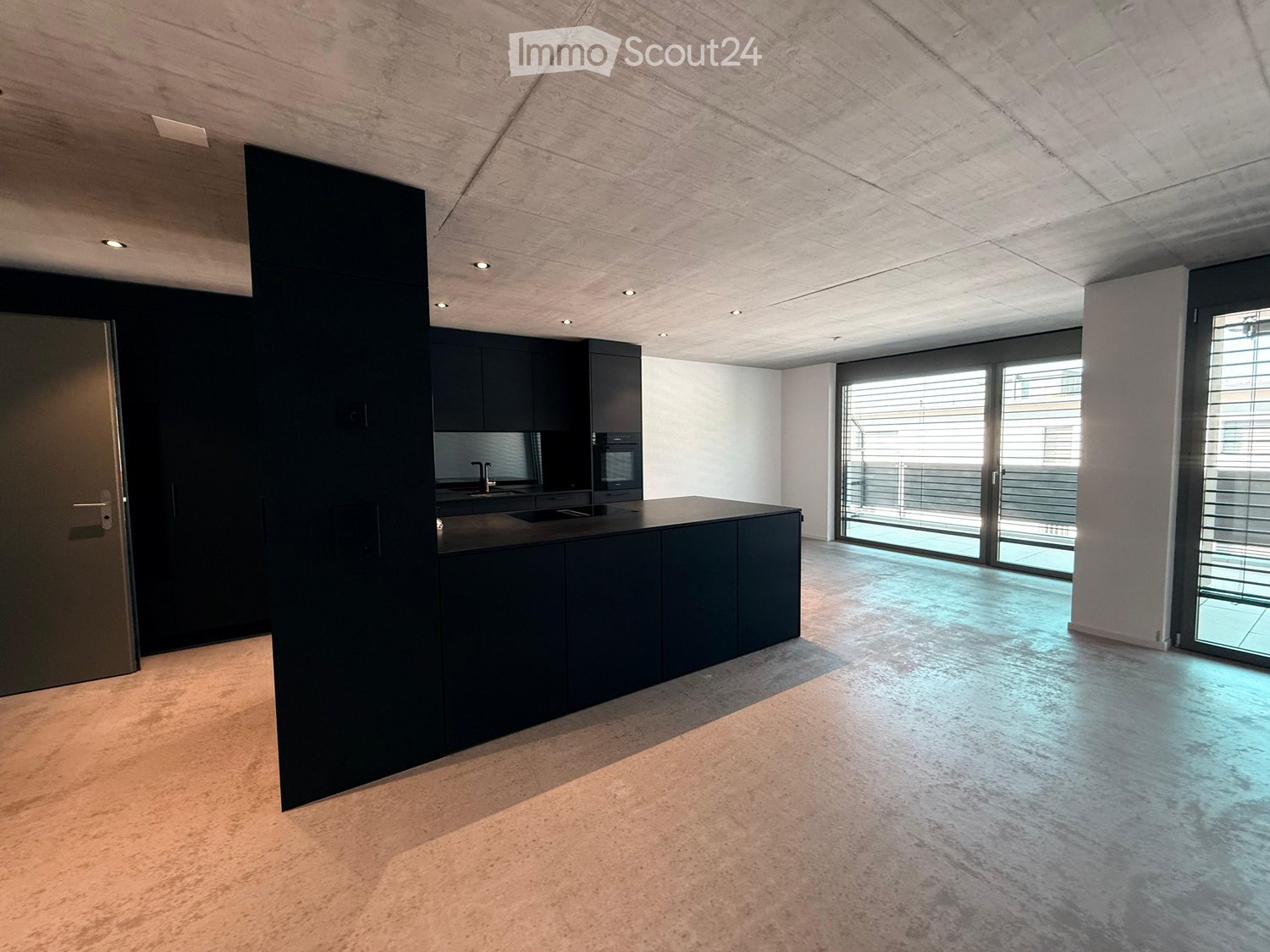 Modern kitchen with dark cabinets, a central island, and large windows leading to a balcony.