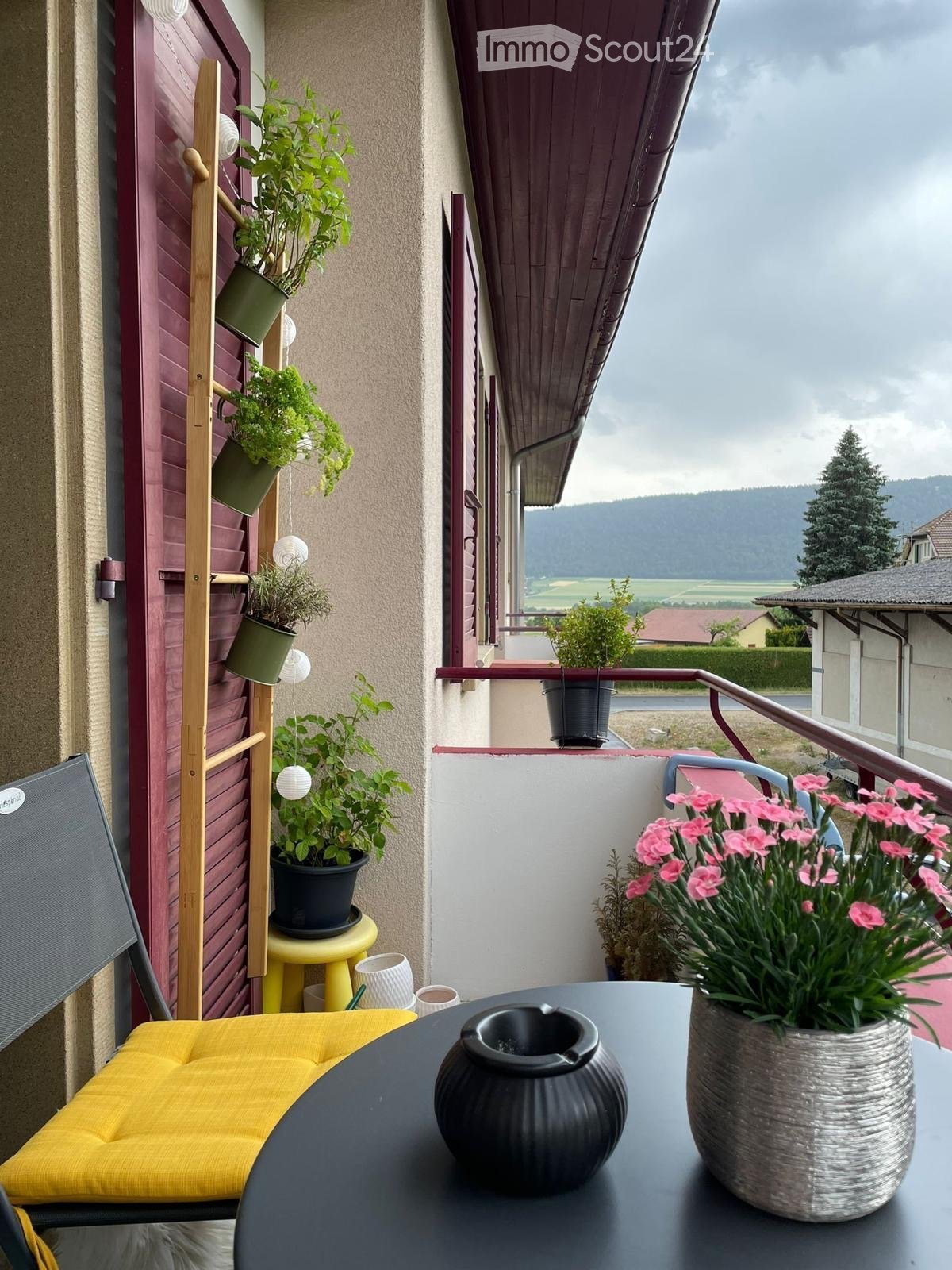 Balcony with a view, featuring a table with vases, a yellow chair, and several potted plants.
