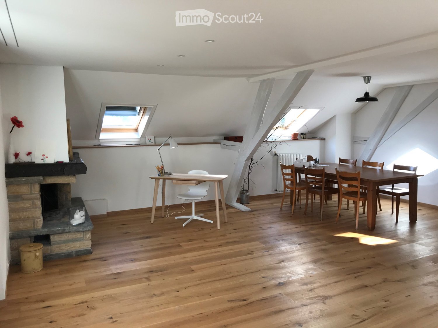 Bright, open room with wooden flooring, fireplace, desk, dining table, and chairs. Skylights provide natural light.