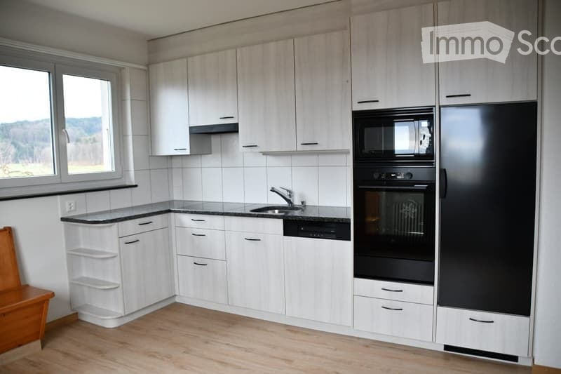 Modern kitchen with white cabinets, black appliances, and a wooden floor. Features a sink, microwave, oven, refrigerator, and dishwasher.