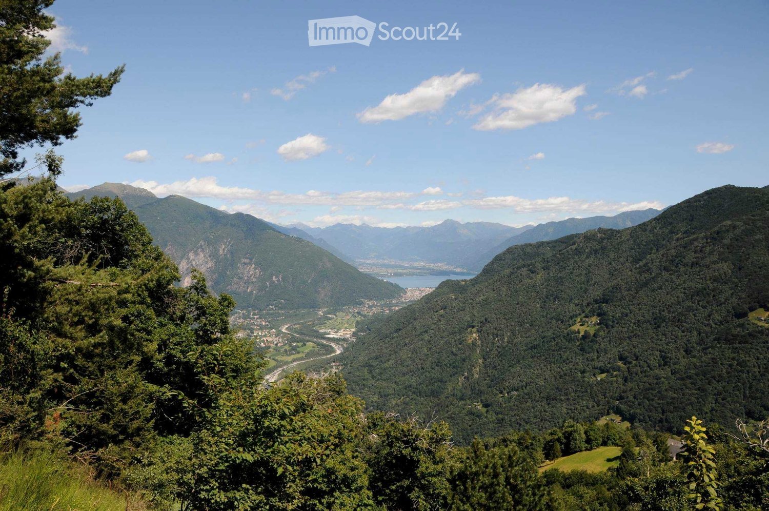 Panoramic mountain view with lush green forests, a lake, and a town nestled in the valley below.