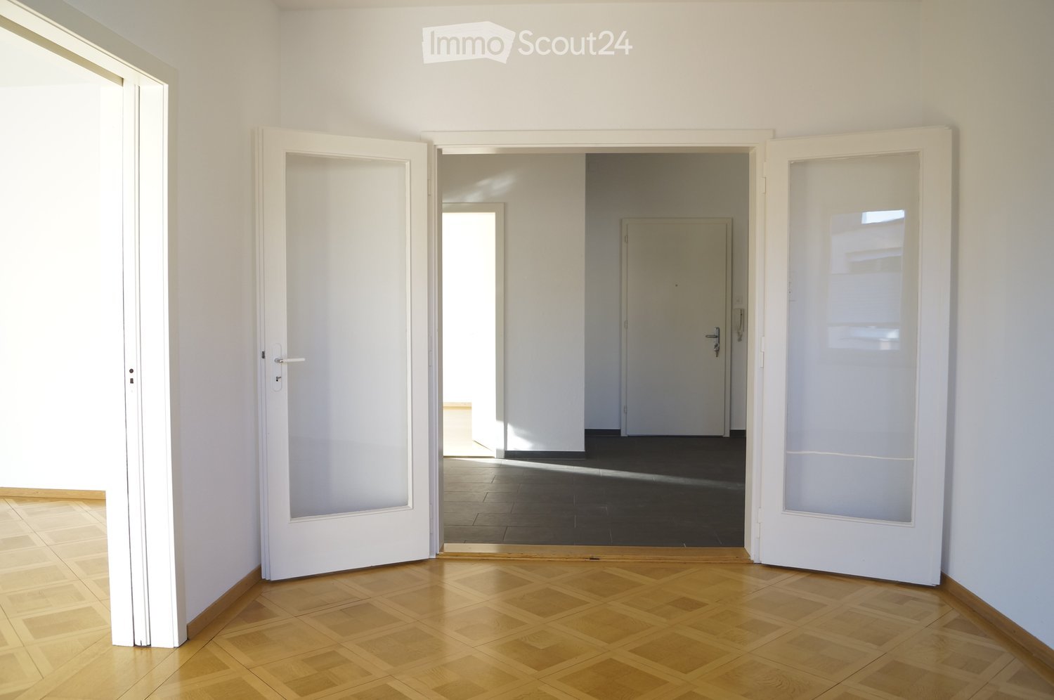 Empty hallway with wooden flooring, white walls, and multiple doors leading to other rooms.