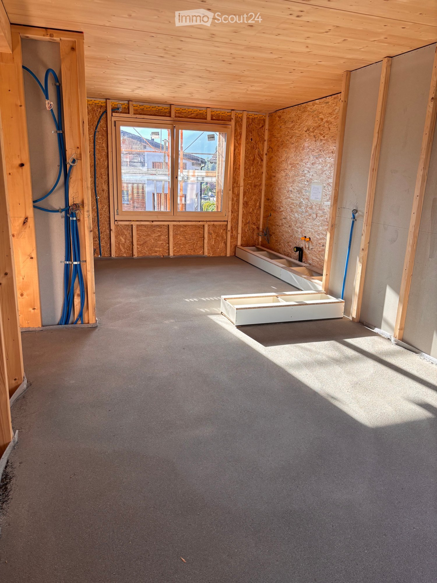 Empty room with unfinished walls, exposed wooden beams, and a large window showing a view of the street.