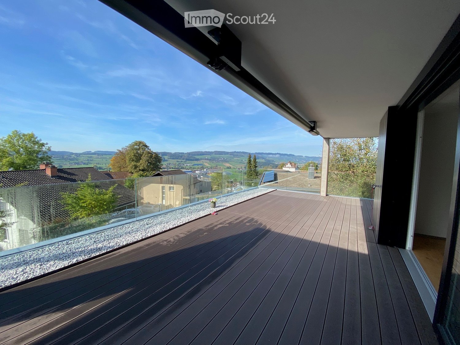 Modern balcony with wooden decking, glass railing, and scenic countryside view.