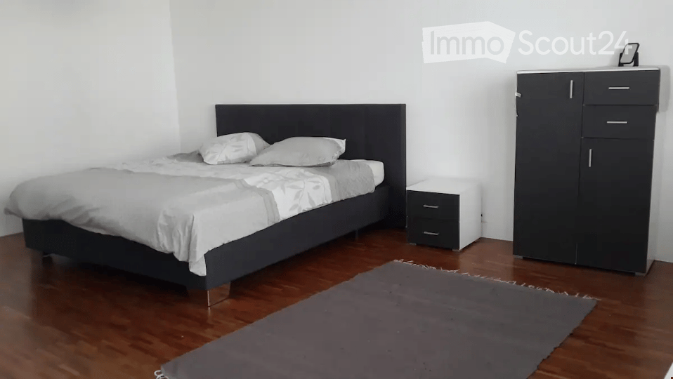 Modern bedroom with a dark wooden bed, white bedding, a nightstand, a wardrobe, and a grey rug on the floor.