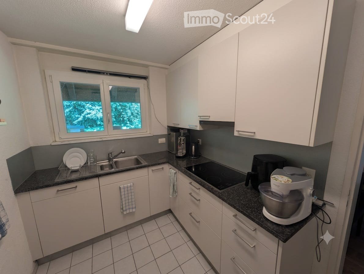 Modern kitchen with white cabinets, dark countertops, and stainless steel appliances. Features a sink, microwave, coffee maker, electric stove, mixer, and plates on the counter.