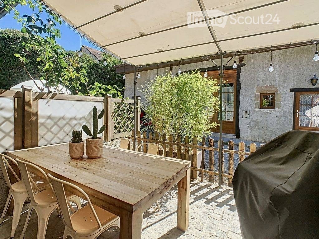 Outdoor patio with a wooden dining table, four chairs, two potted plants, a covered canopy, and a wooden fence.