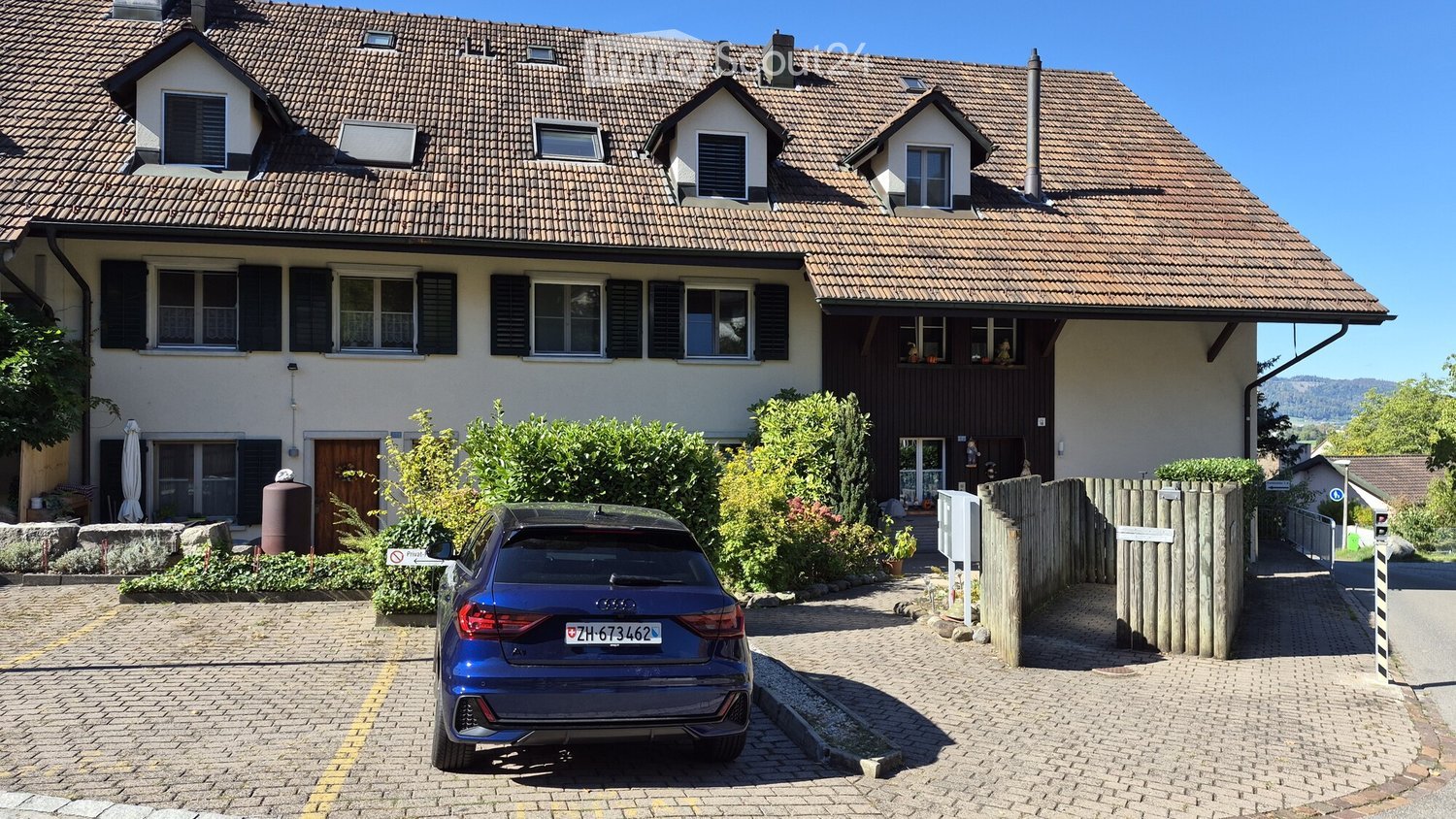 Two-story house with a tiled roof, multiple windows, and a garage. A blue car is parked in the driveway.