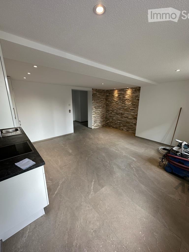 Empty room with white walls, tiled floor, and a small black countertop with a sink. A stone accent wall and a doorway lead to another space.