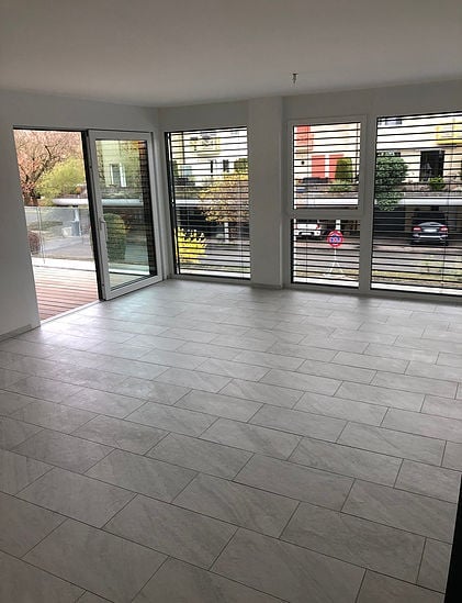 Empty room with large windows, tiled floor, and sliding glass doors leading to a balcony.