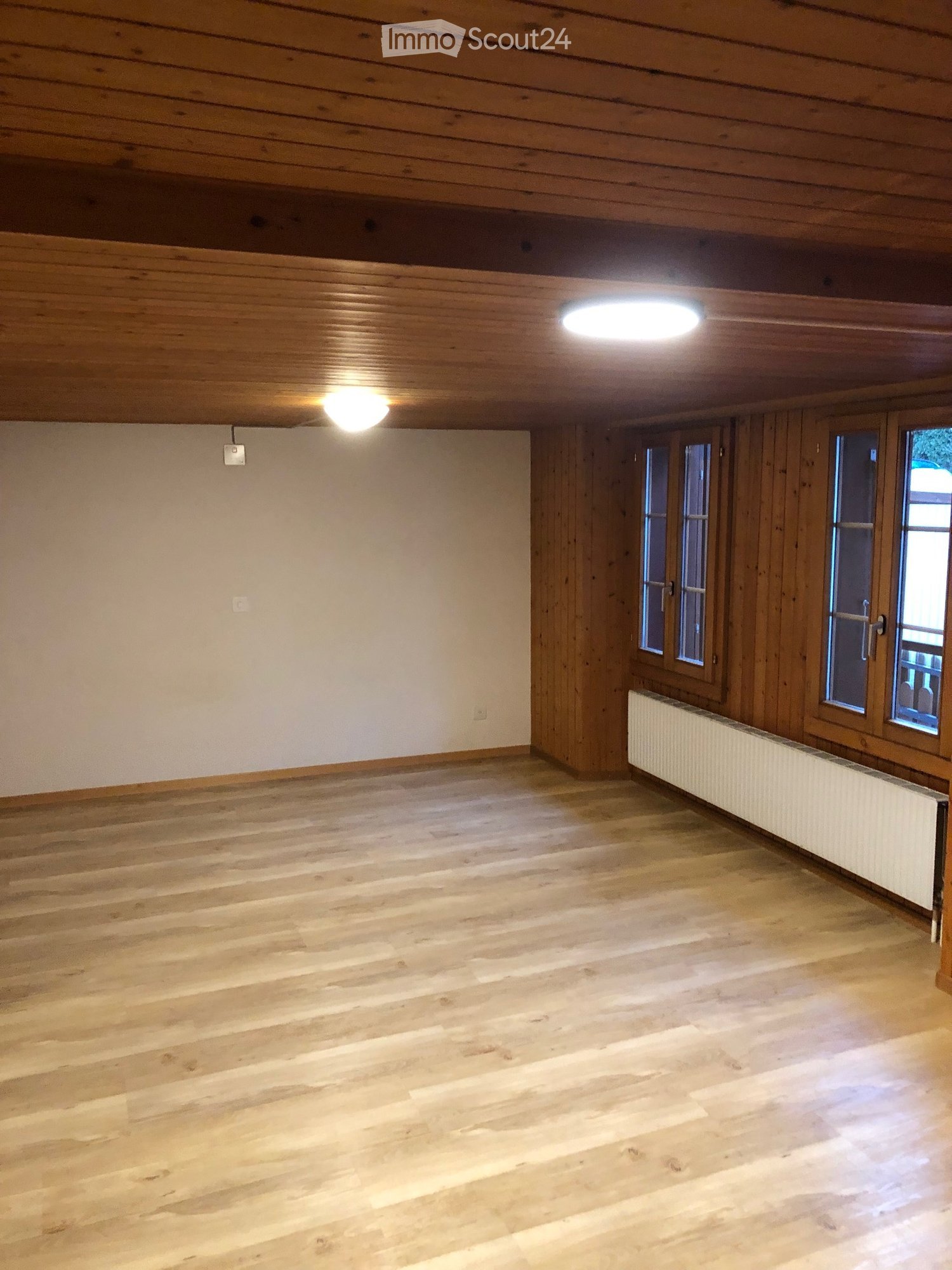 Empty room with wooden floors, wooden walls, and large windows. No furniture or equipment present.