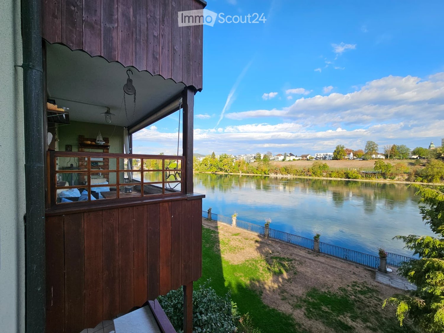 Wooden balcony overlooking a serene river with a scenic view of the surrounding landscape and town.