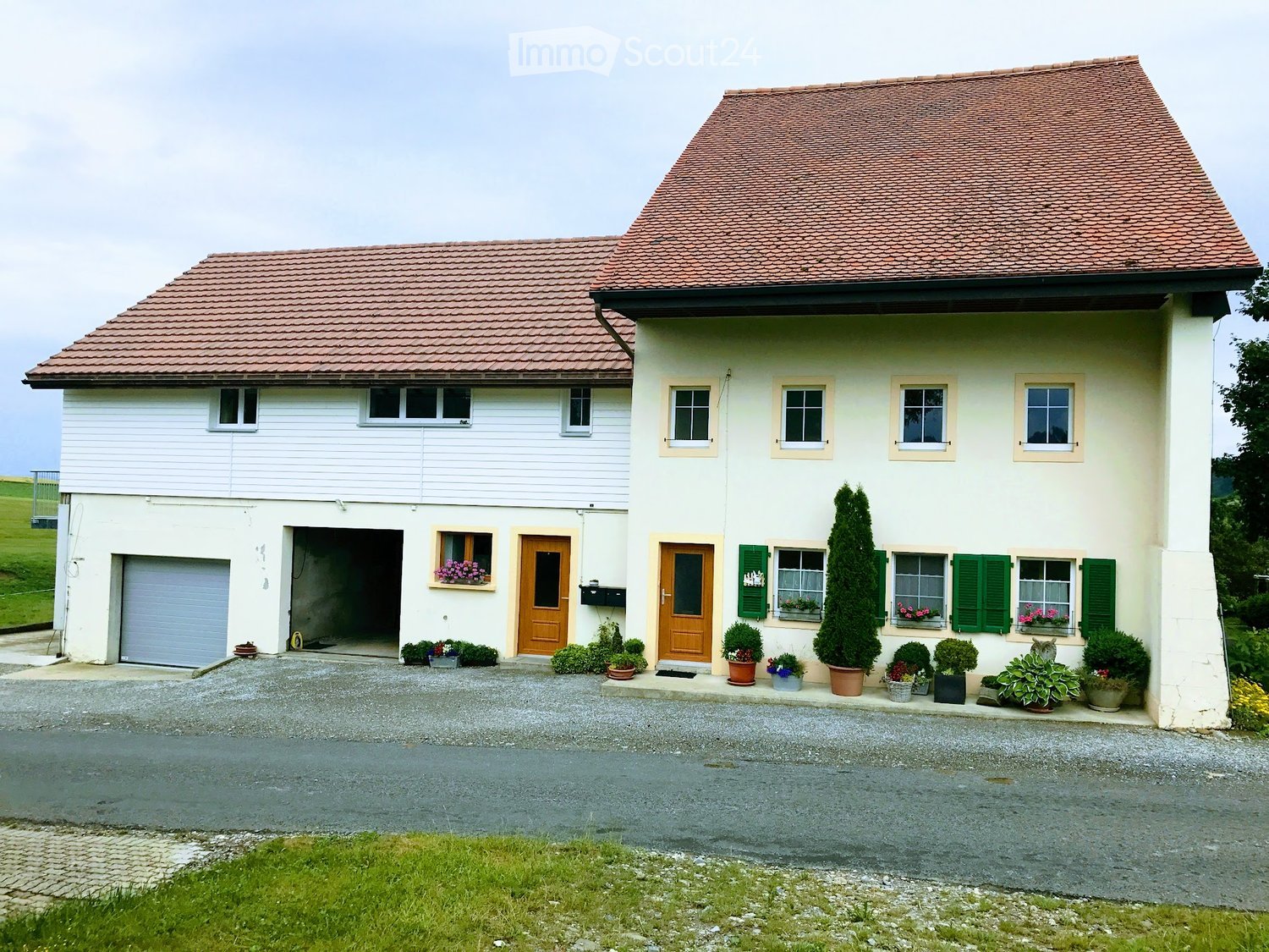 Two-story house with red-tiled roof, white siding, green shutters, garage, and flower boxes.