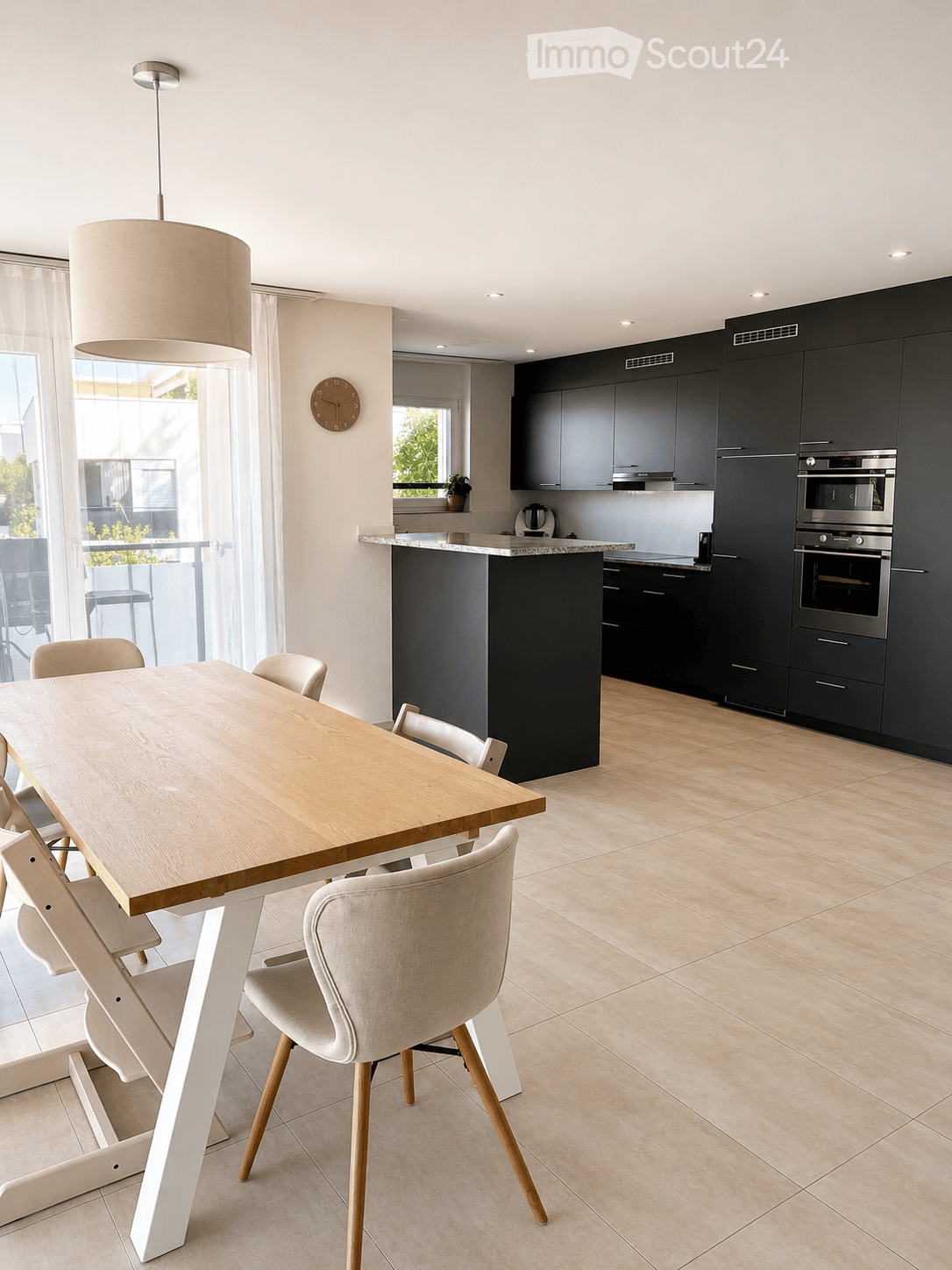 Modern kitchen with dark cabinets, a central island, a dining table with chairs, and built-in appliances including an oven and microwave.