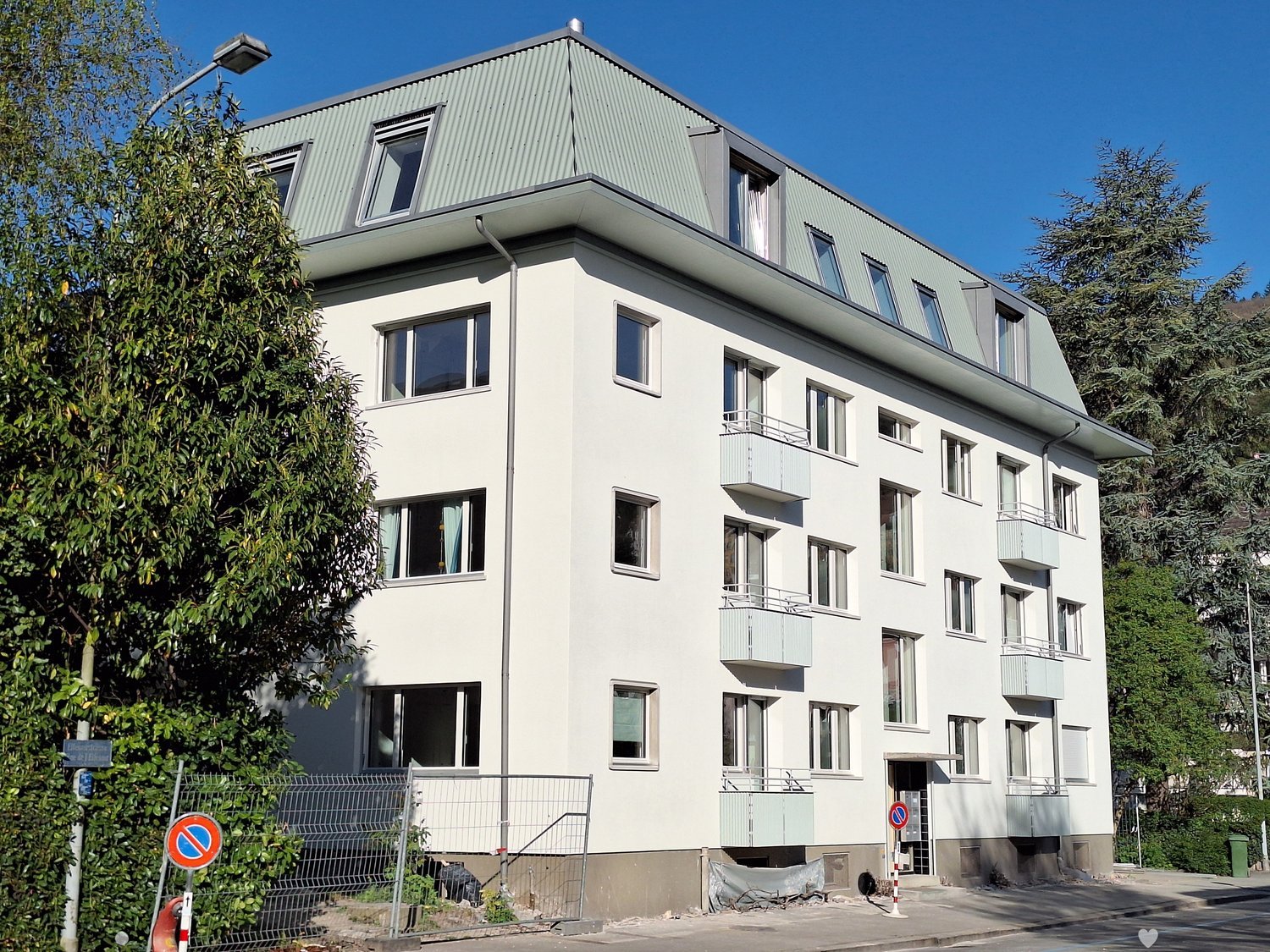 Four-story residential building with white facade, multiple windows, and balconies on the upper floors.