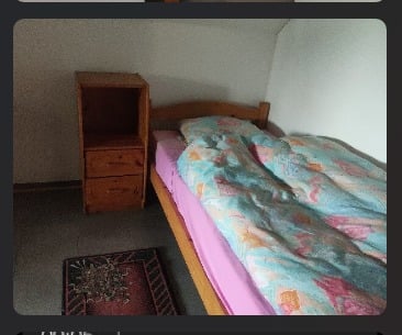 Small bedroom with a single bed, colorful quilt, wooden nightstand, and a small rug on the floor.